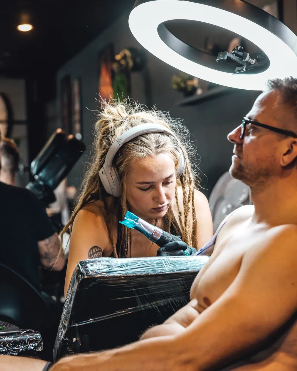 En artist tatoverer en kunde under en ringlampe
