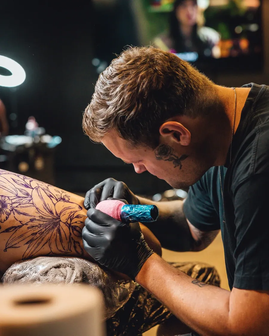 En artist tatoverer et ben med et blomstermotiv